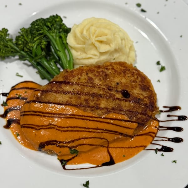 Crispy fried chicken with orange sauce, balsamic glaze, mashed potatoes, and broccolini on a white plate.