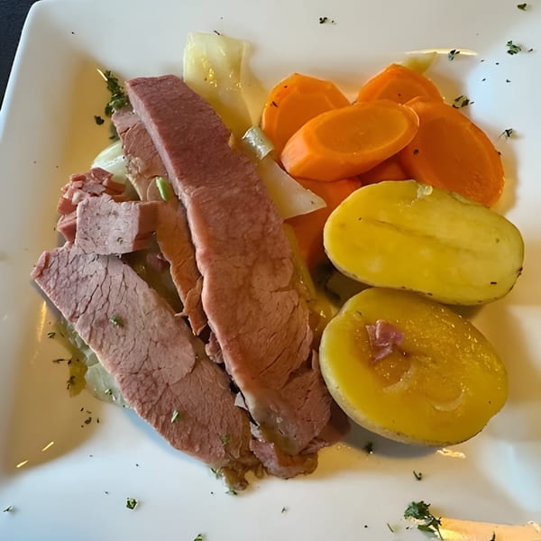 Platter of sliced corned beef, cabbage, carrots, and potatoes, garnished with herbs.