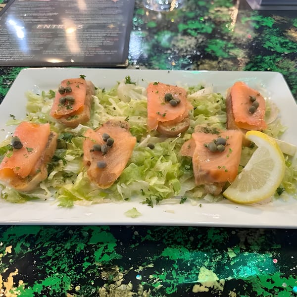 Smoked salmon appetizers with capers and parsley on a bed of lettuce with a lemon wedge.