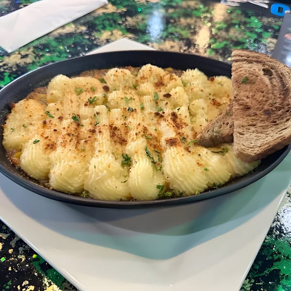 Shepherd's pie with piped mashed potato topping and a slice of brown bread in a black dish.