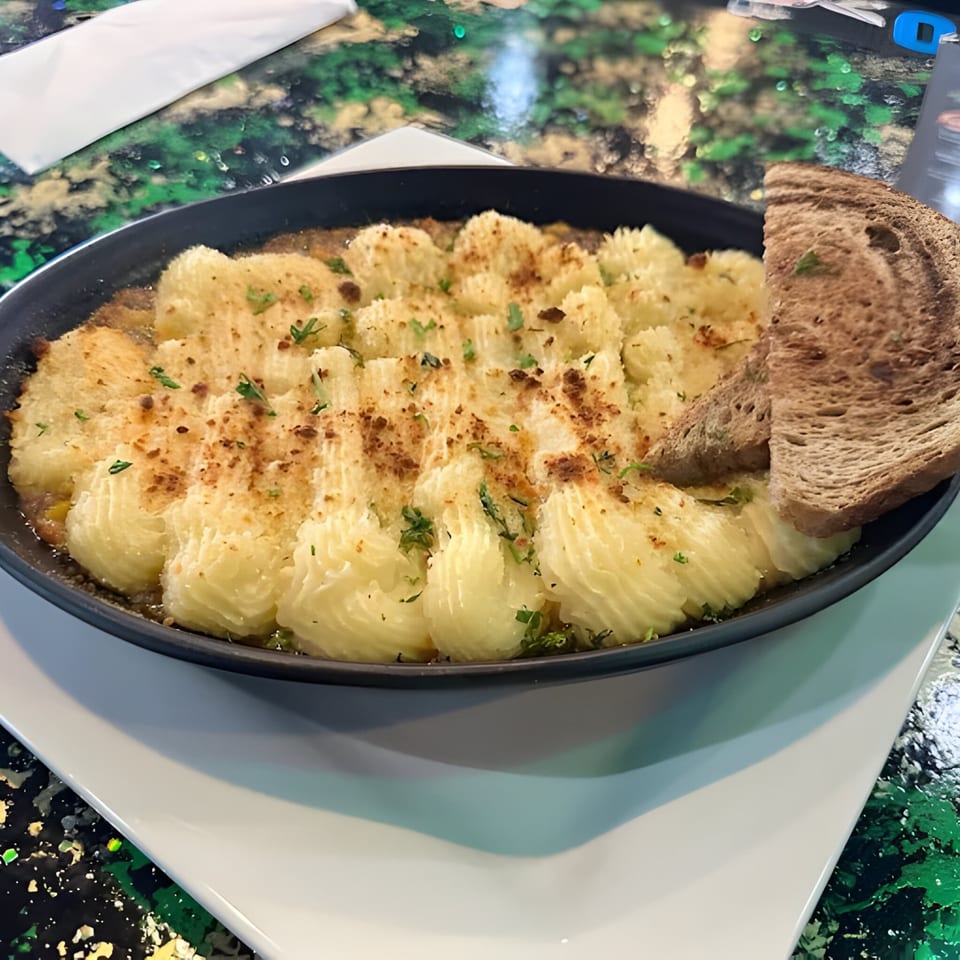 Shepherd's pie with piped mashed potato topping and a slice of brown bread in a black dish.