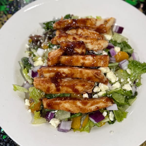 Grilled chicken salad with mixed greens, red onion, feta cheese, and orange segments on a white plate.