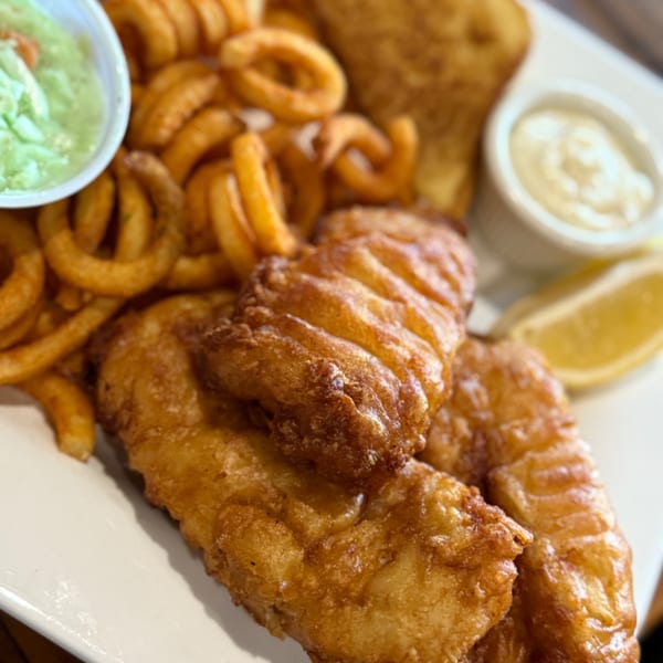 Golden-brown fish and chips with curly fries, tartar sauce, and a lemon wedge.
